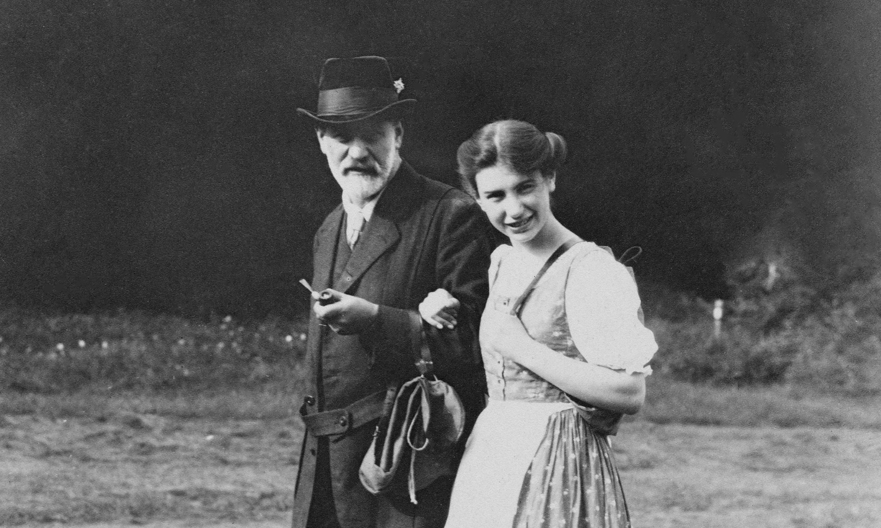 Black and white photograph of Sigmund and Anna Freud walking arm in arm and looking at the camera